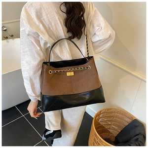 Détail de suède marron mat et cuir matelassé noir avec une chaîne dorée chic