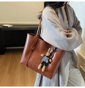Detail of a brown leather tote bag featuring a cute rabbit charm and gold logo lettering
