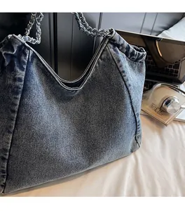 Detail view of denim tote bag with interwoven metal chain strap and soft washed fabric