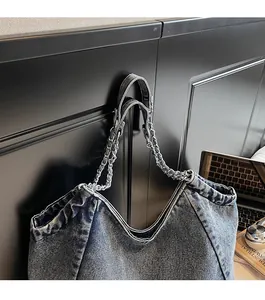 Detail of durable denim tote bag with woven metal chain strap and pleated finish