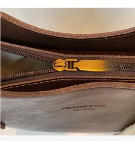 Macro shot of a smooth metal zipper and brand embossing on a brown leather hobo bag