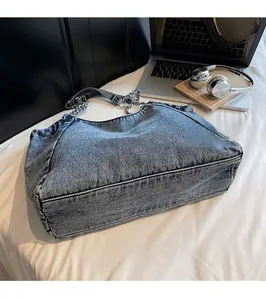 Detail view of deep blue denim tote bag with silver chain strap on a white surface