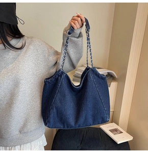 Detail of blue denim tote bag featuring silver chain straps in a casual lifestyle setting