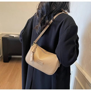 Sac bandoulière minimaliste en cuir grainé beige avec logo embossé porté par mannequin