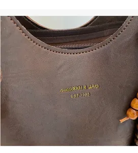 Close-up of brown leather tote bag with gold logo and decorative wooden beads detail
