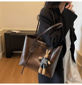 Close-up of vintage brown leather tote bag with long shoulder strap and rabbit charm