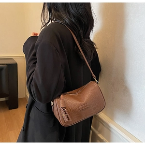 Sac à bandoulière en cuir marron porté par un mannequin en blazer noir avec sangle large