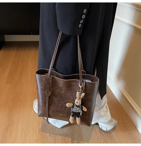 Detail of dark brown leather tote bag featuring a cute rabbit charm and gold logo lettering