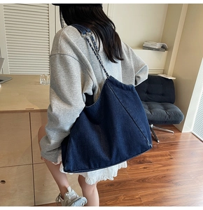 Side view of a vintage denim tote bag with chain strap worn by a model in an indoor setting