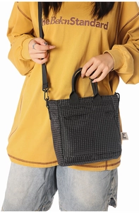 Detail of black grid crossbody bag worn by model with yellow sweatshirt and denim