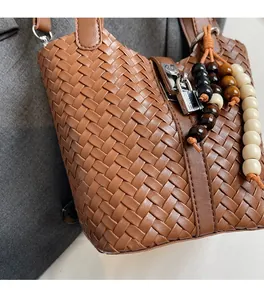 Détail d'un sac seau tressé marron avec fermoir métallique et breloque en perles de bois