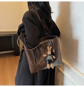 Detail of vintage brown tote bag with fashion lettering and rabbit charm on shoulder