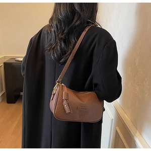 Détail d'un sac hobo en cuir grainé marron caramel avec plaque dorée mode