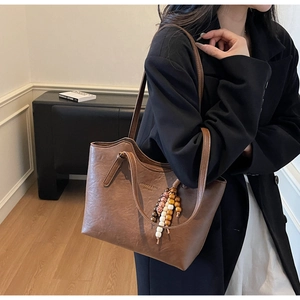 Detail view of brown vintage leather tote bag with ethnic bead tassel and brand logo