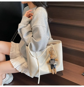 Close-up of white leather tote bag with a cute rabbit charm on a wooden background