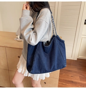 Detailed view of large blue denim tote bag with silver chain strap shown on person