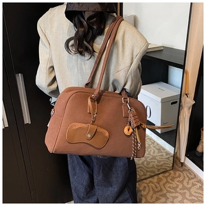 Dettaglio borsa tote marrone opaca con ciondoli e pochette sulla spalla della modella