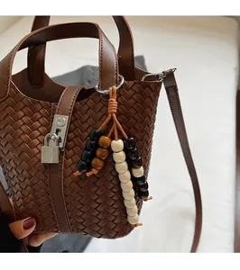 Détail d'un sac seau en cuir tressé avec breloque en bois et cadenas métallique chic