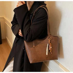 Detail of vintage brown leather tote bag featuring a beaded pendant and minimal gold logo