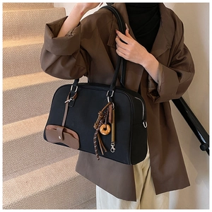 Dettaglio della grande borsa tote in nylon nero con manici in pelle marrone e ciondoli