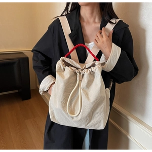 Zaino beige con coulisse e manico intrecciato rosso mostrato su una modella