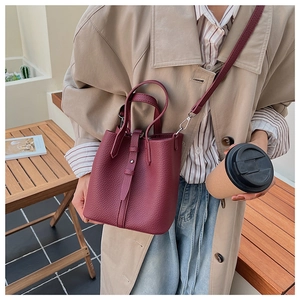 Detail of burgundy textured leather bucket bag with top handle and adjustable strap