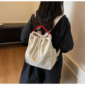 Dettaglio dello zaino in tela beige con manico intrecciato rosso indossato da una modella