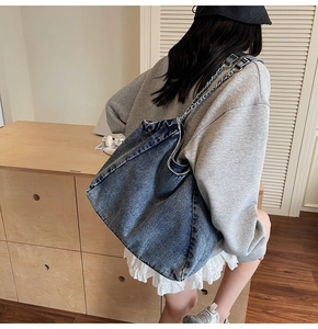 Detail of vintage denim tote bag with metal chain strap worn by a model in a room
