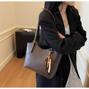 Detail of vintage brown tote bag with beaded pendant and golden logo on textured leather