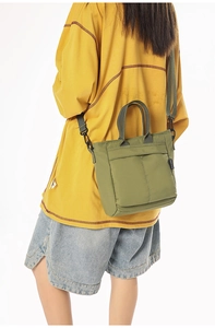 Army green nylon tote bag on yellow sweater showing shoulder strap and casual style