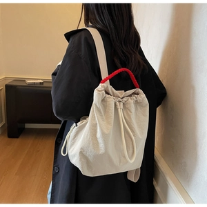 Vista dettagliata dello zaino in tela beige con coulisse e manico intrecciato rosso