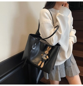 Close-up of black leather tote bag with a brown rabbit charm and printed text