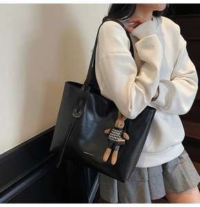 Detail of black leather tote bag with a cute rabbit charm and fashion logo text