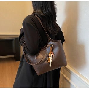 Macro view of dark brown faux leather tote with colorful beaded charm and gold lettering