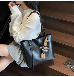 Detail of black faux leather tote bag with a houndstooth rabbit charm and textured finish