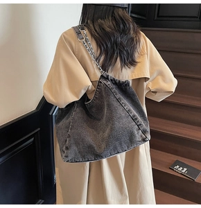 Detail showing high-capacity grey denim hobo bag with metal chain strap on a model