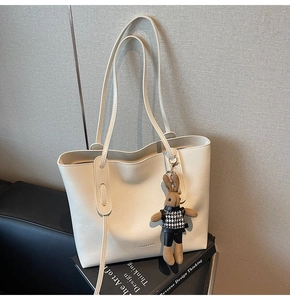 Detail of a beige leather tote bag with a small bunny charm on a black sofa