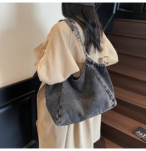 Detail of a grey denim tote bag with chain strap worn by a model in a warm lifestyle setting