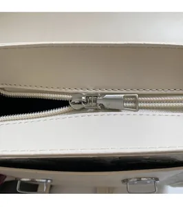 Detail shot of smooth silver metal zipper pull on a cream-colored textured leather bag