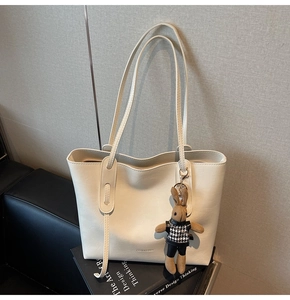 Close-up of beige tote bag with long straps and cute brown rabbit charm on leather sofa
