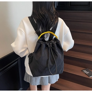 Dettaglio dello zaino in nylon nero con coulisse, manico in tessuto giallo e tasche laterali