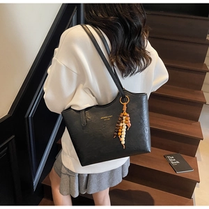 Close-up of black leather tote bag with brand logo and decorative wooden bead charm