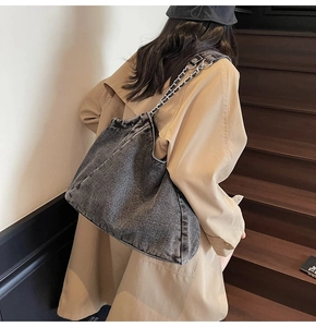 Detail of grey washed denim hobo bag with silver chain strap worn with trench coat