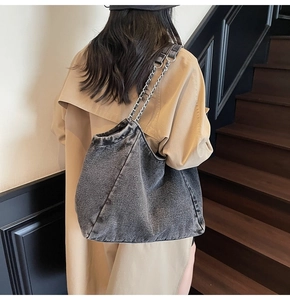 Detail of vintage grey denim tote bag with metal chain strap worn on khaki trench coat