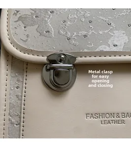 Detail of elegant cream leather bag showing embroidery and silver metal hardware closure