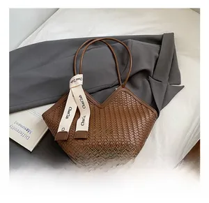 Close-up of brown woven tote bag featuring decorative ribbon on a soft white bedding