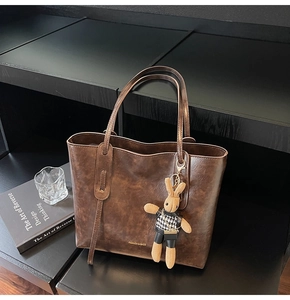 Detail of vintage brown leather tote bag featuring a creative bunny plush pendant and text