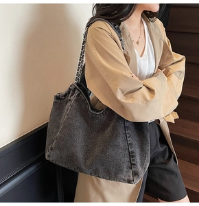 Detailed view of the dark denim tote bag with silver chain strap shown on a model