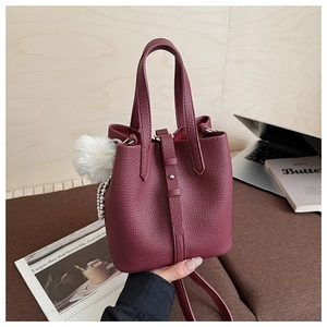 Detail of burgundy lychee grain leather bucket bag with fuzzy pompom and pearl chain