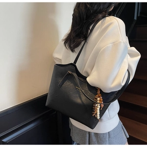 Detail of black PU tote bag with gold logo lettering and rustic wooden bead accessory